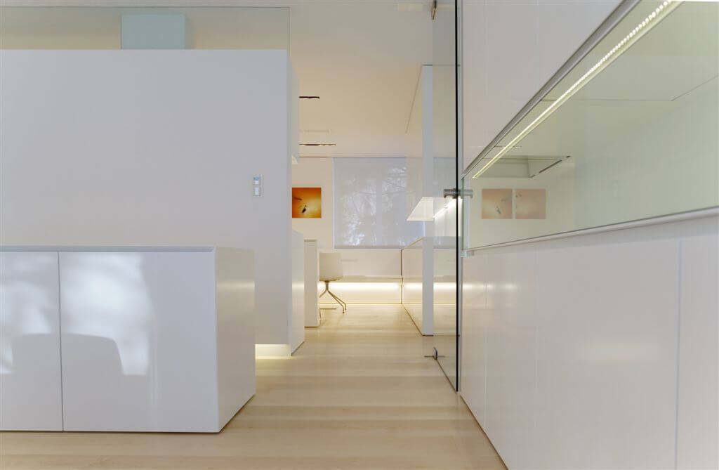 Hallway featuring large expanses of glass set against smooth white surfaces, with corner office area in background.