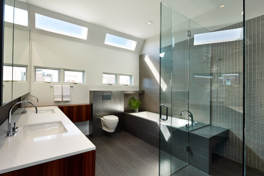 Primary bathroom features all-glass shower, white countertops, red wood cabinetry, and dark wood floor extending to bath surround.