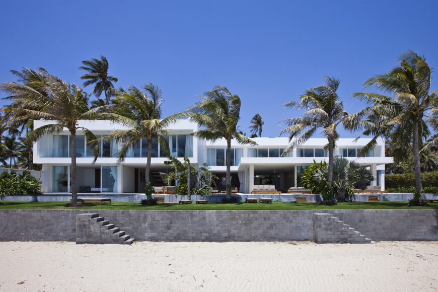 From the beach we see the raised construction wall protecting the home and surrounding lawn from the elements and erosion. Every exterior wall on this facade is floor to ceiling glass.