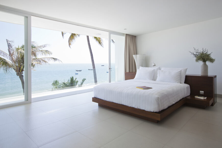 Primary bedroom featuring another combination desk and bed frame in rich dark wood, overlooking the ocean via floor to ceiling sliding glass.