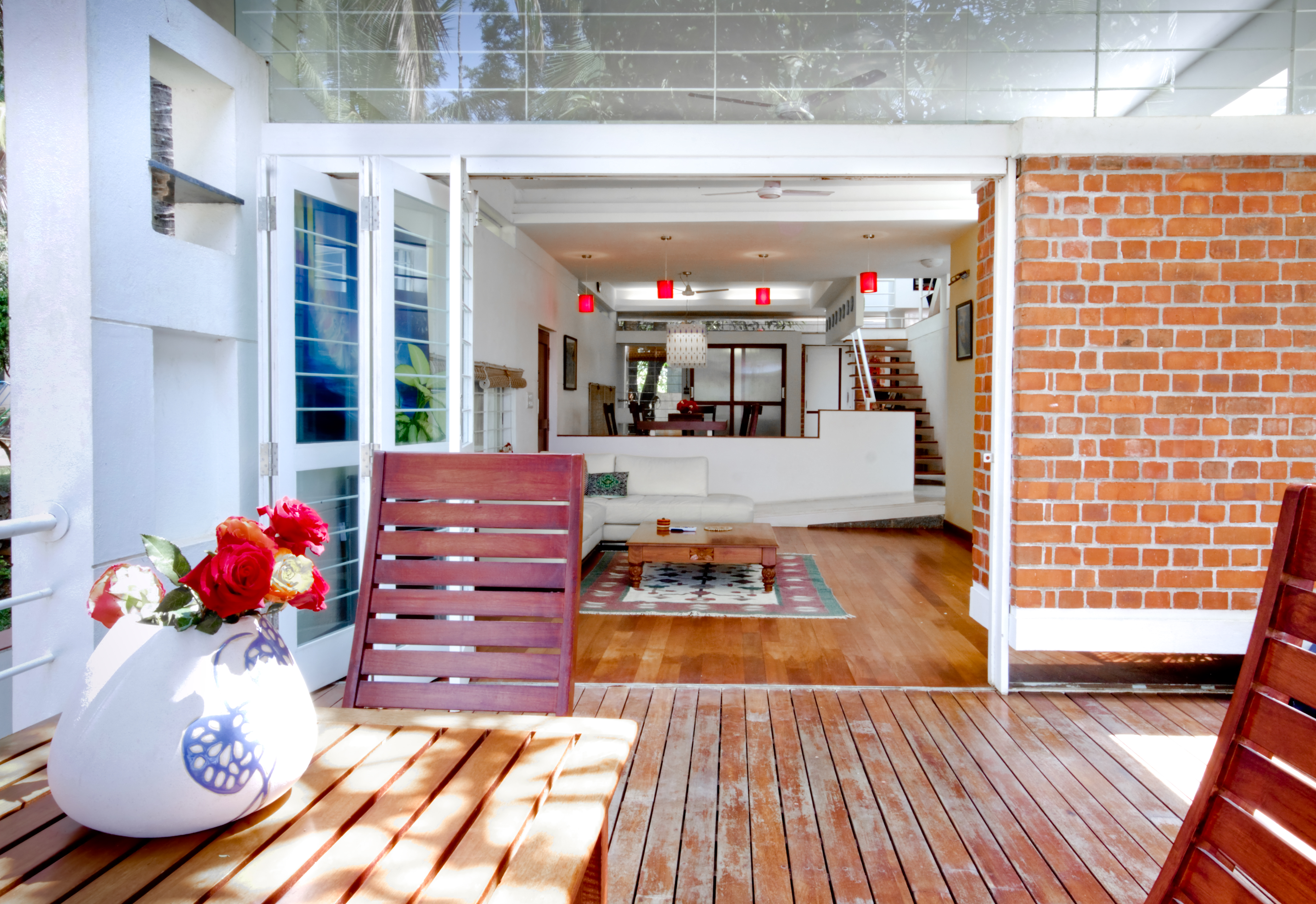 View into the living room from patio. Lush natural hardwood flooring throughout is paired with white walls and L-shaped sectional.