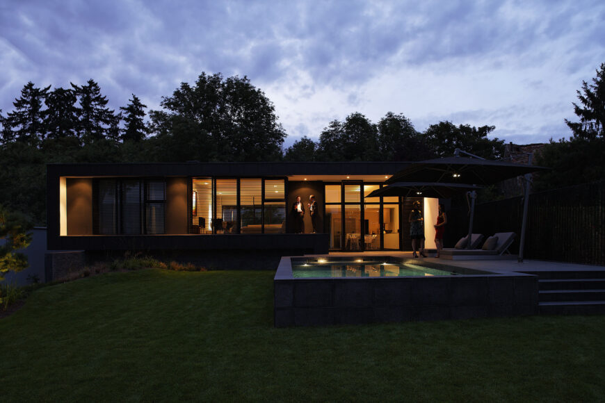 Pulling back a bit, we can see the entire patio structure, extending from the foundation. Subtle lighting embedded in the roof overhang softly illuminates the pool area, reflecting the interior lighting.