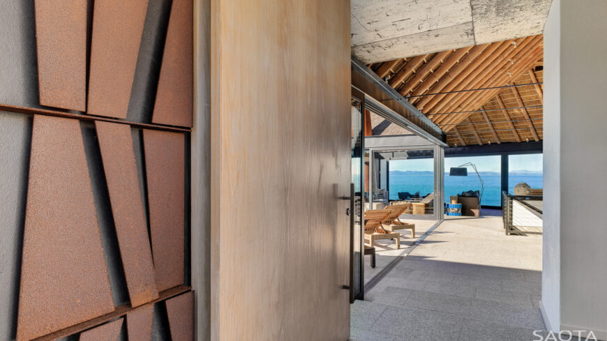 Through the main entrance, we see the mixture of wood, stone, and structural I-beams framing the interior. Glass exteriors throughout highlight the spectacular views.