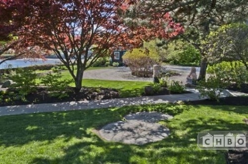 The manicured front garden has a stone walkway that winds through the property and is shaded by ornamental and native trees.