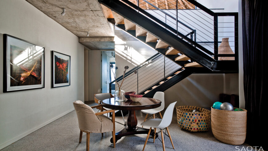 From the lower level, we see the central I-beam framed staircase. A small dining area in this open space gives way to hallways leading to the private bedroom areas.