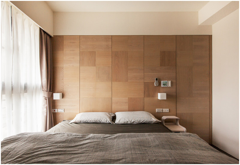 The bedroom does have one small, slim nightstand on the right, but otherwise the room has minimal furniture. A large window with airy curtains is on the left wall.