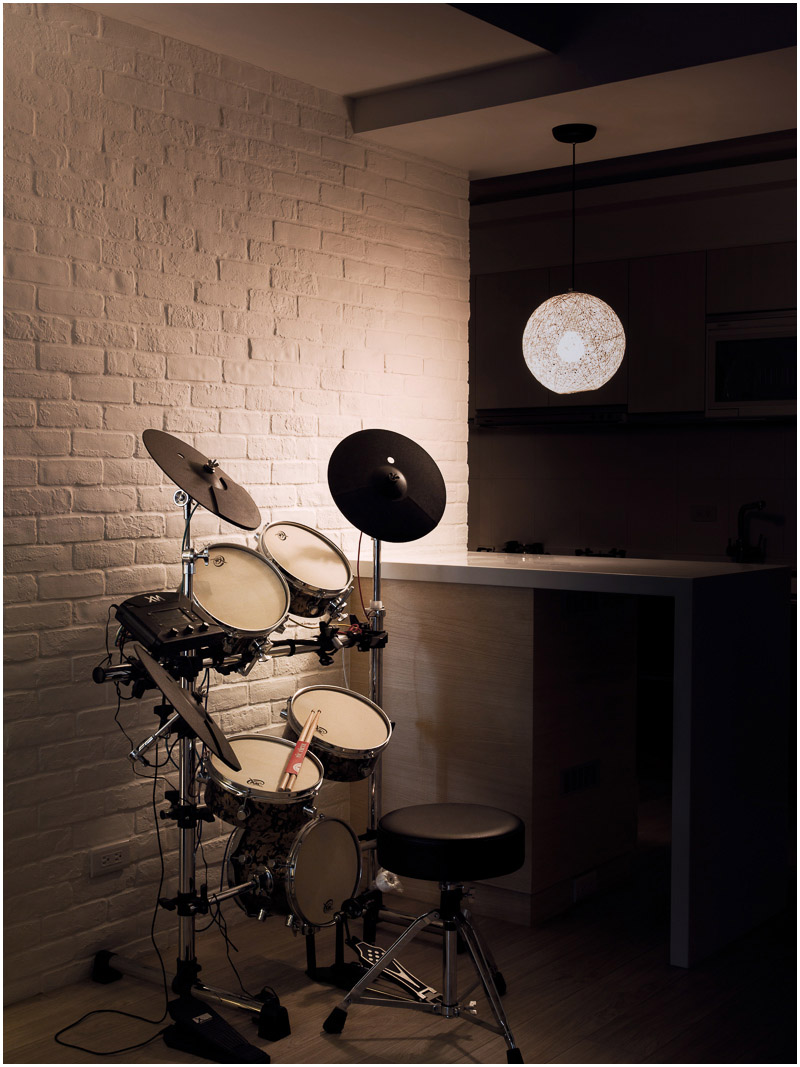 On one side of the small galley kitchen is another music nook, this time containing a drum set. A small circular pendant light hangs above the kitchen bar.