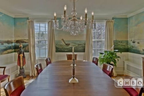 The formal dining room has an immense antique hardwood table with red upholstered seats, white crown molding, wainscoting and an elegant crystal chandelier. The walls are painted with scenes of the sea, which can be seen through the windows of the room.