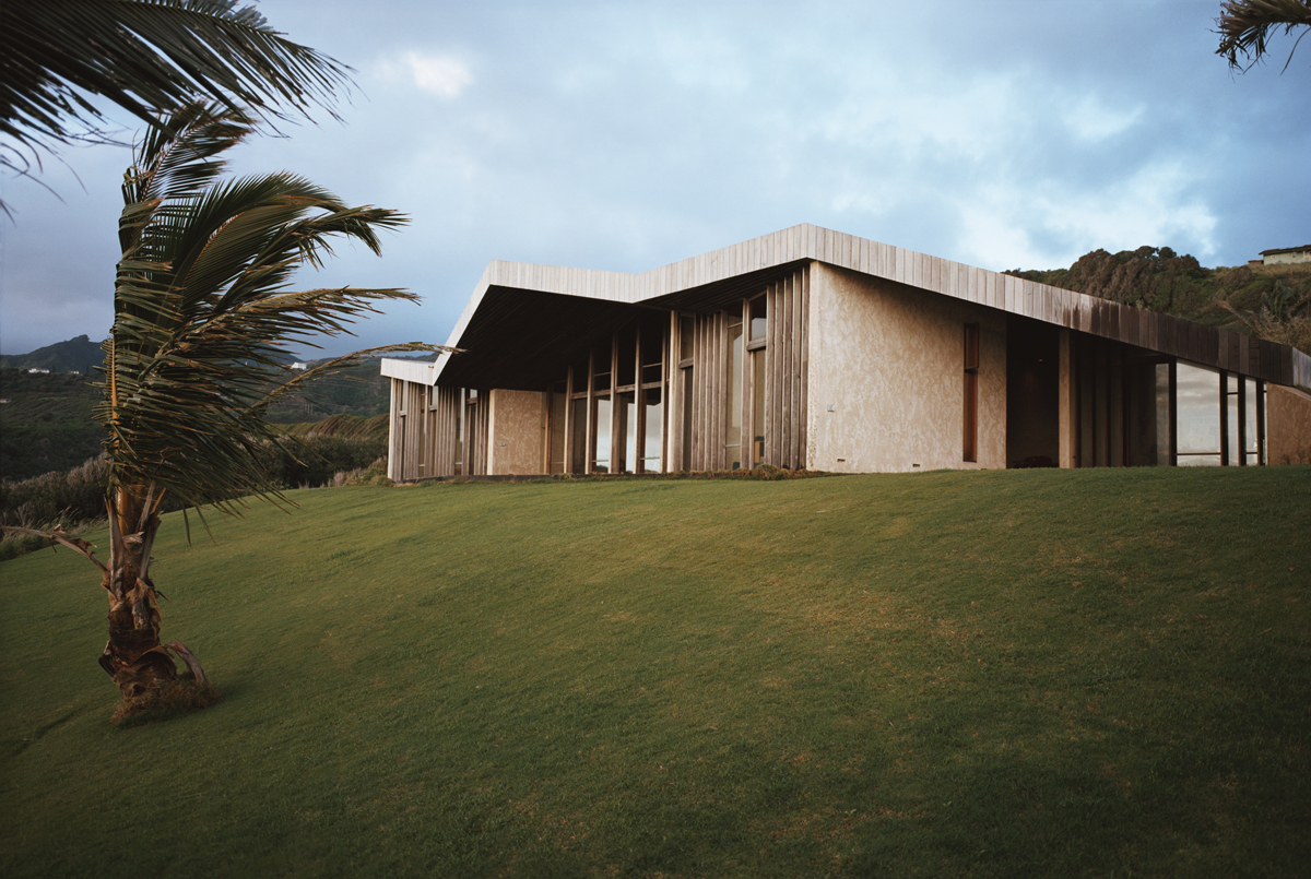 The ocean facing side of the home is a series of windows, unbroken except for slim vertical wood beams. The outline of the folded wooden sky deck roof are clearly appreciated from this angle. 