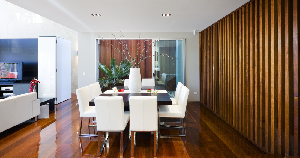 Dining space accented with wooden panel wall along with glossy hardwood flooring. It has a dark wood dining table with white chairs and a lovely centerpiece.