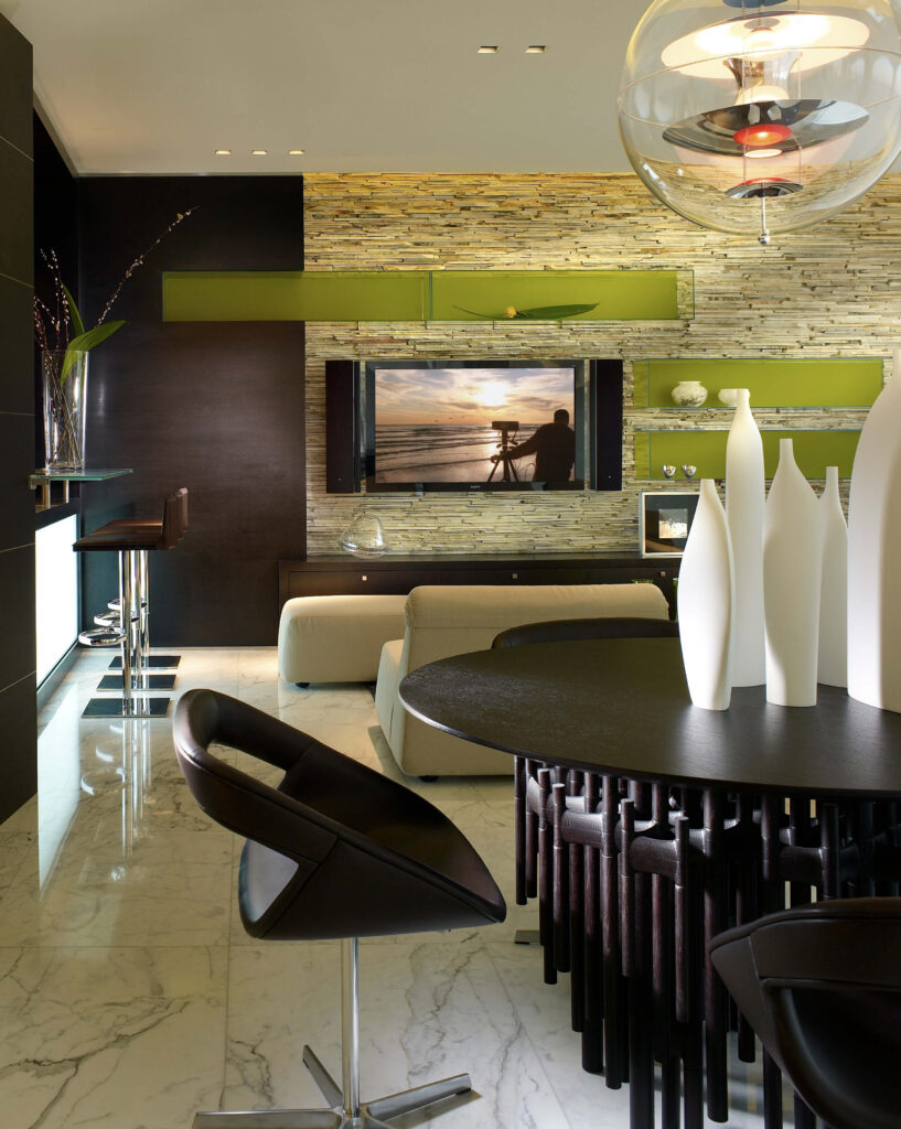 The bold semi-transparent green floating shelves, paired with the very modern light fixture over the small dining area makes for a casual family room for entertaining smaller groups. On the left there is a wet bar.