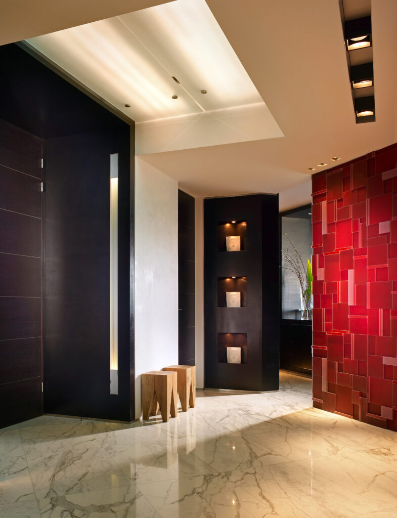  The entryway of the home has clothespin shaped wooden stools beside the door and another red polygon accent wall. Another wall has small lighted alcoves.