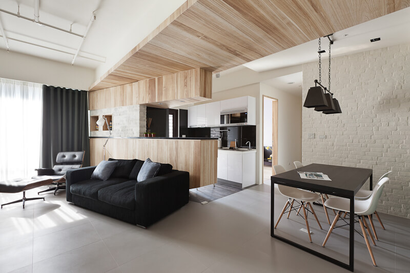 The central open plan space includes a living room and this kitchen and dining area. Black hued furniture contrasts with the white walls and light toned wood paneling.