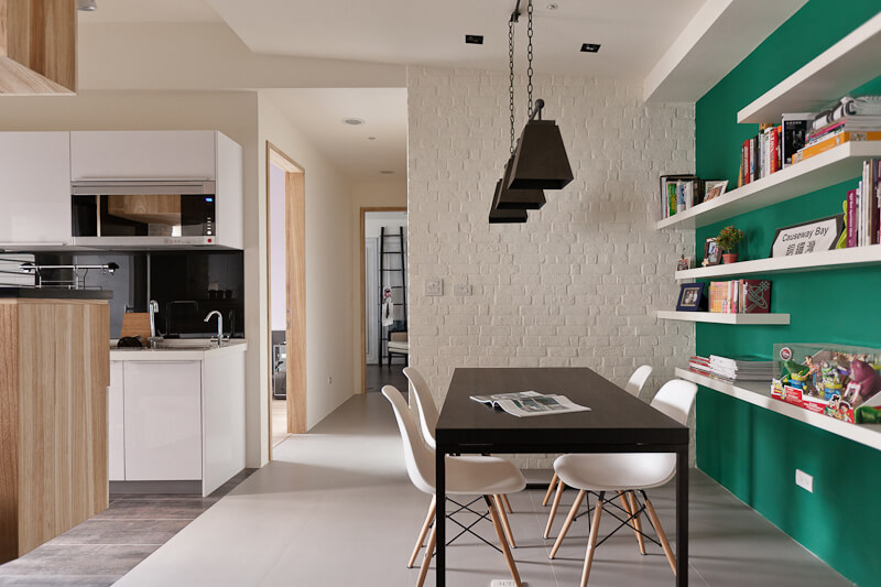 The dining area features a major splash of color in the form of this green wall at right, backing a set of minimalist white shelves.