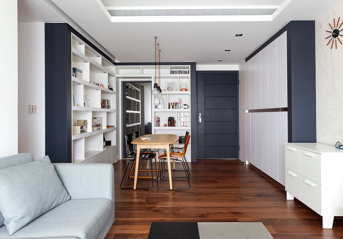 White and black dining space with hardwood flooring and built-in cabinet and shelves. It is lighted with small pendants that hung from the white ceiling.