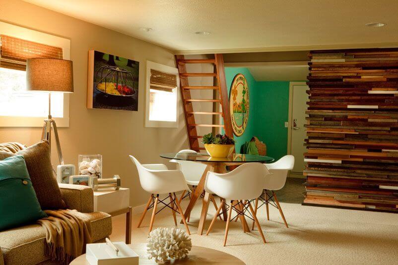 Down a set of stairs is the family room, with a small circular table with white bucket chairs and a layered wood half-wall.