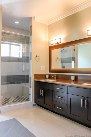 The full bathroom for the children is equally as simple, with a dark dual vanity and bronzy countertops. The shower stall is closed off by a glass door and contains the bathtub as well.