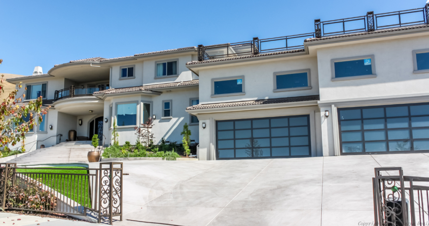 A wrought-iron gate surrounds the sprawling property of this enormous home. The gate leads directly up to either garage. Above the garages we can see a rooftop terrace.