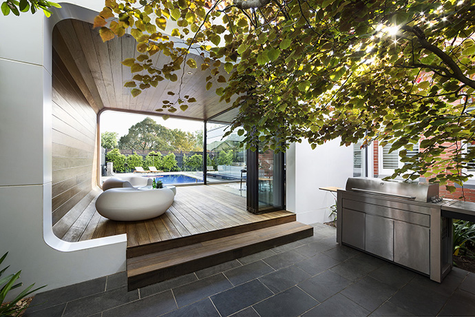 A 3-seasons room sits behind the house, attracting attention with its incredible round walls and natural wood. The glossy white of the walls contrasts with the dark wood that curls from the floor and up onto the ceiling.