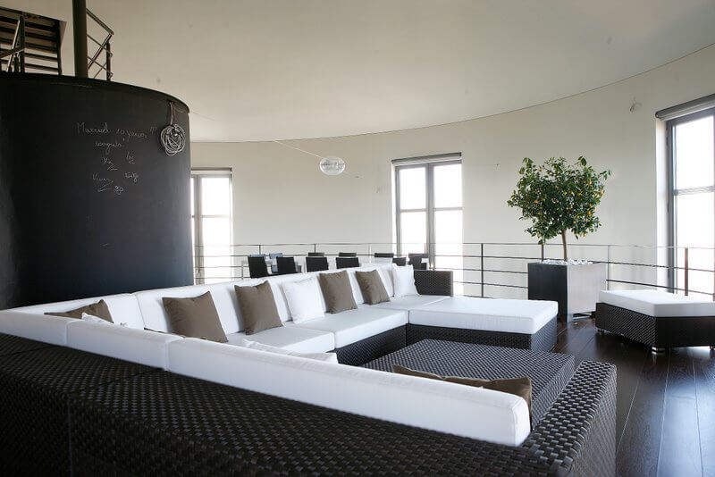 On the opposite side of the chalkboard staircase is a massive black wicker sectional topped with pristine white cushions and accented with dark taupe pillows. An ottoman can be pushed up against the chaise or used as extra seatin