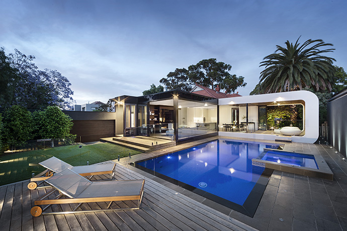 The back of the home consists of unique glazing, exposing the kitchen, living room, dining room, and 3-seasons room. The landscaping mimicks the modern design from the backside of the house, and pulls it into the patio– modernizing the outside with grey concrete and a brilliant blue pool.