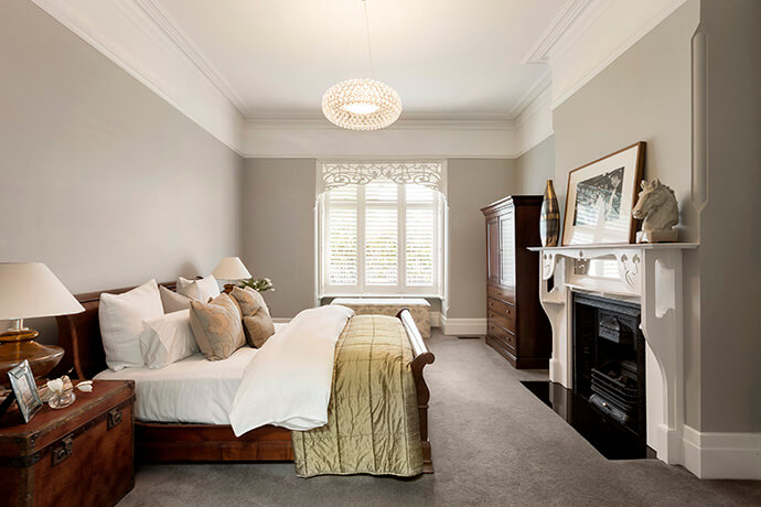 The original part of the home contains elegant furnishing, like this bedroom equipped with a gorgeous vinyl mantle. An intricate design in the window and a delicate light fixture ties the fashionable scheme together.