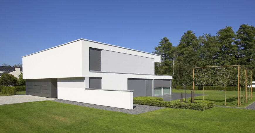 Standing over an expansive pristine green lawn, the house is wrapped in a subtle patio matching the grey shades of the exterior cladding. Shading seen at left provides incremental privacy.