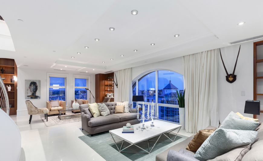 This dazzling living room offers up plenty of light and striking views of the surrounding city, mountains, and ocean. The pale blue and golden accents are reminiscent of the sky at daybreak.