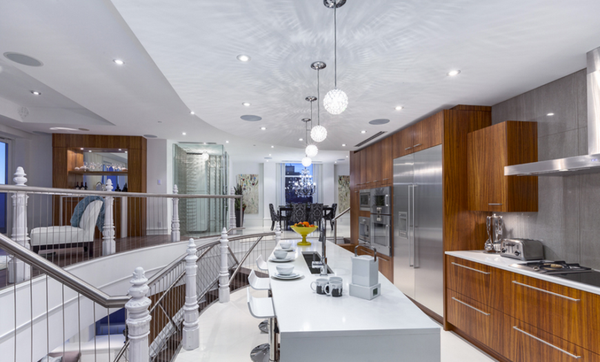 The beautiful kitchen features Gaggenau stainless steel appliances and a huge island bar and prep space. The cabinetry continues the use of Mozambique millwork and is accented by a lovely grey marble backsplash. In the center of the island is a narrow prep sink that shows an excellent use of space. The use of the warm wood in the kitchen helps to break up the bright white of the rest of the second floor.