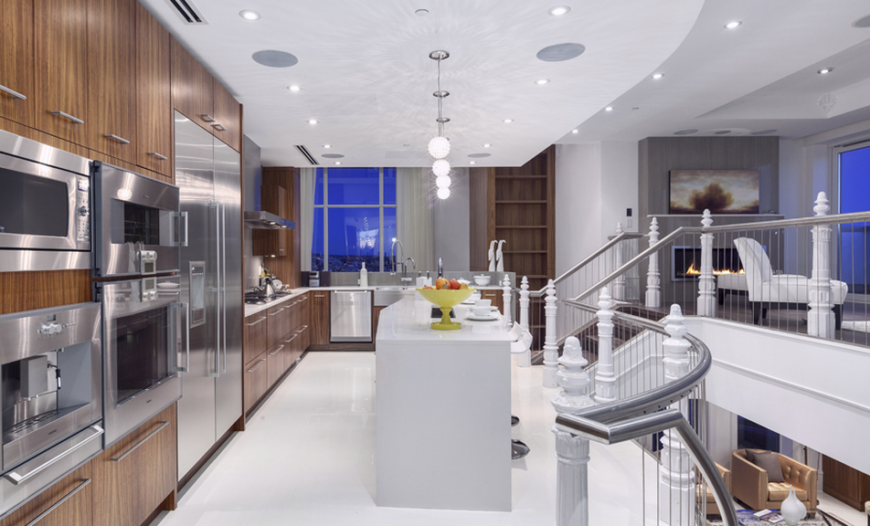 The far end the kitchen offers more counter space and overlooks the open room of the library below. To the left is a better view of the striking appliances set into the cabinets. The pendant lights over the island cast wonderful patterns on the ceiling.