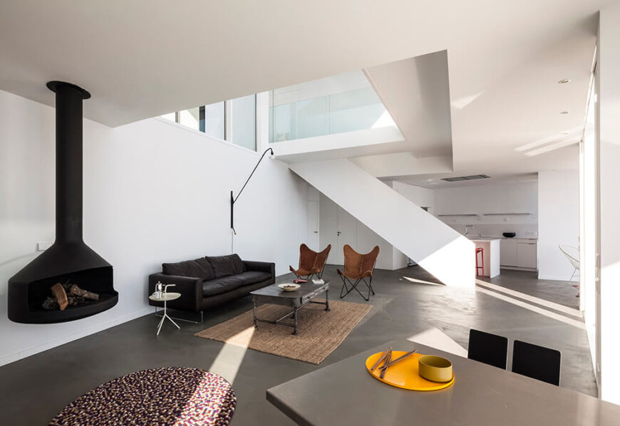 Taking a right off of the stairs leads us into the spacious, minimalist living room, complete with a simple raised wood-burning fireplace. Butterfly chairs and a leather sofa are positioned for an optimal view.