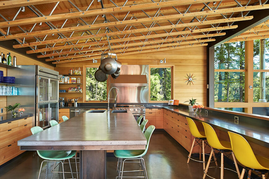 The kitchen is the first room to greet guests. Outfitted to accommodate large gatherings, the concrete topped kitchen island is often used as a dining table. The warm wood of the cabinetry adheres to the rustic retreat theme achieved by the rest of the house. The half wall of the kitchen bar opens up to, and looks out over, the living room area and allows for an unimpeded view of the lake.