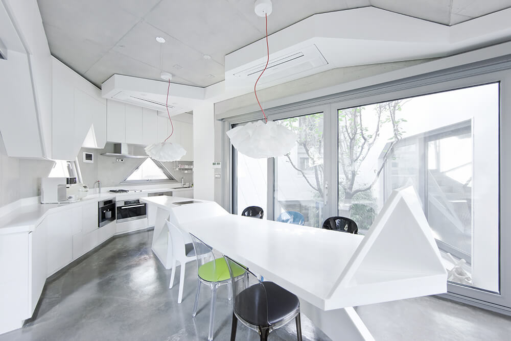 White dining room features a lengthy modern dining table that extends with the breakfast island accented by multi-colored chairs over concrete flooring. 