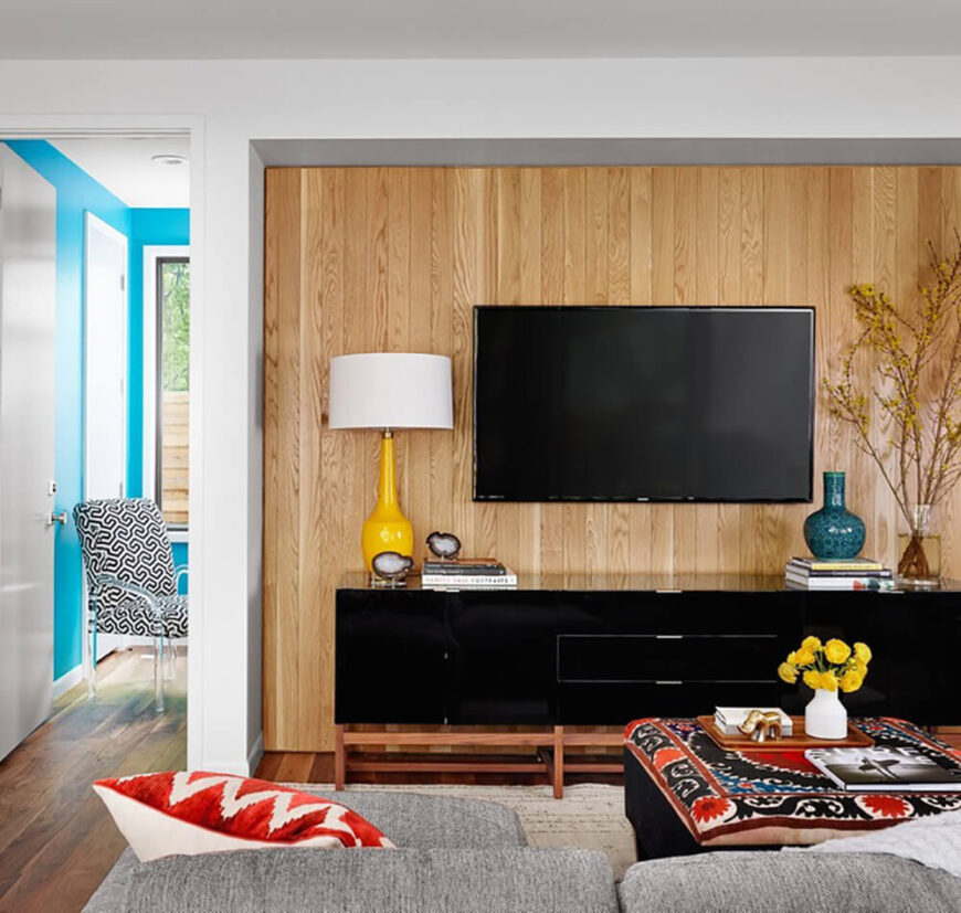 The family room features a similar splash of bright natural wood, backing the sleek black entertainment center. In the next room, we can see sky blue walls, another fresh wrinkle in the interior design of this home.