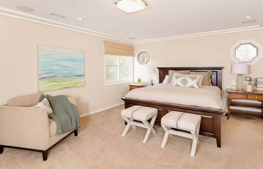 Cream and beige are neutral colors that keep your bedroom appealing to both men and women. The bed is dressed up by two small seats in front of the rich wood of the bed frame. A simple watercolor landscape painting brings color into the room.