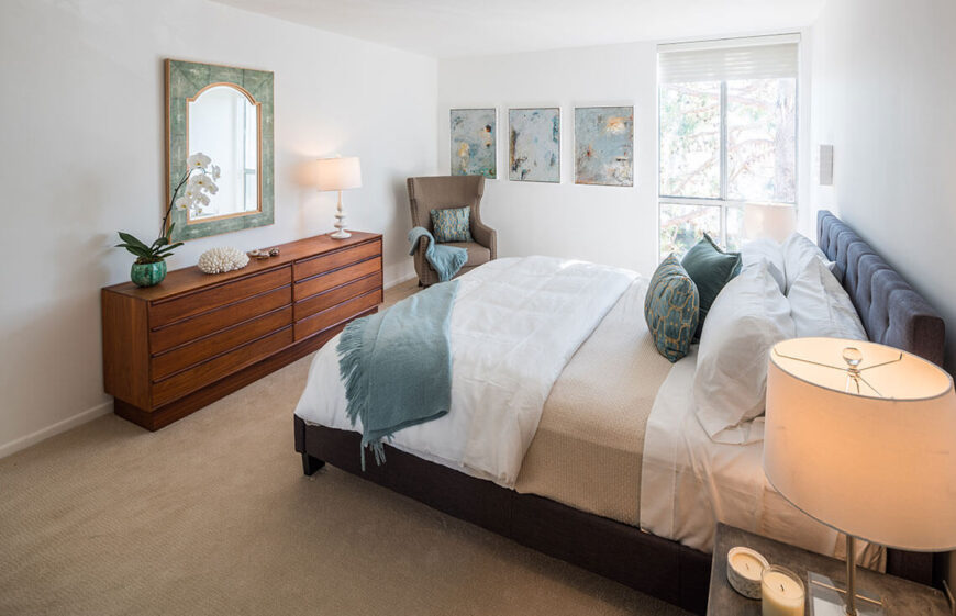 The bedroom is seen from a different angle, highlighting the decorative mirror and small displays on the dresser. Exotic and beachy elements are combined to give the bedroom a sense of a vacation getaway.