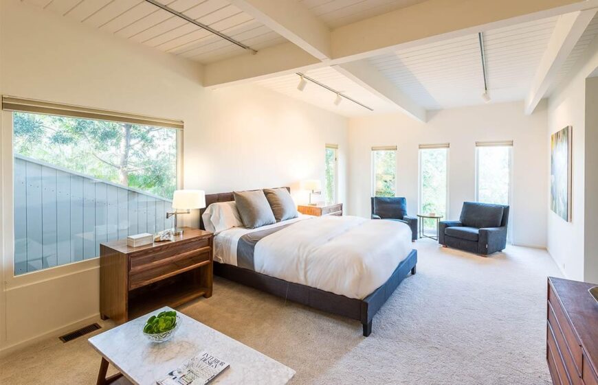 This bedroom is spacious and includes a wealth of windows, which are all unshaded, letting as much light in as possible. Bedside lamps are also included and turned on, for extra light. The walls are in a light, neutral color, with color pulling the eye to the bed. 