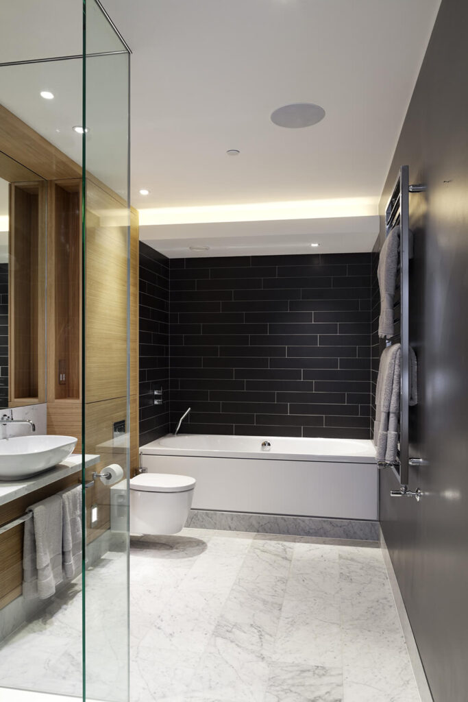 The bathroom is awash in high contrast, tactile elements, with black tile walls, rich natural wood cabinetry, marble flooring, and a floating vanity with vessel sink.