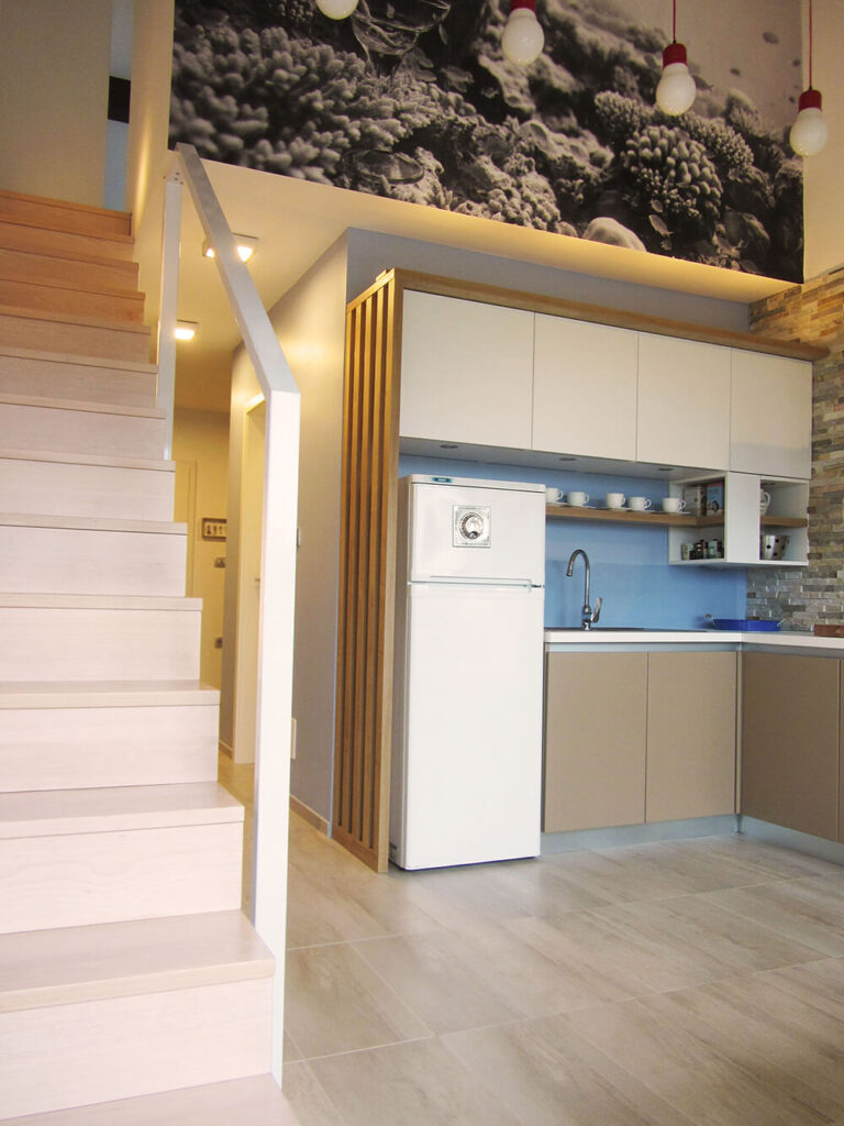 The entry hall ends in the kitchen area, which has been fully renovated with sleek, minimalistic cabinets. The blue wall, backsplash, and an adjacent layered stone facade bring warmth into the simple design.