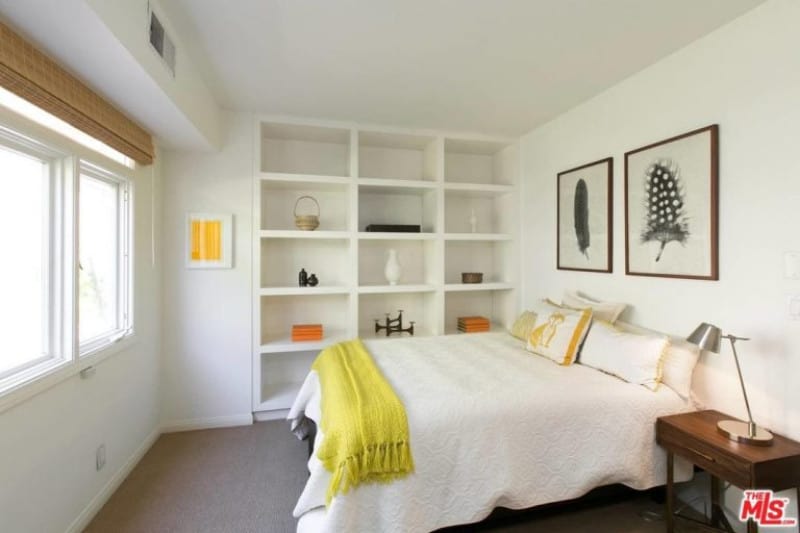 Neutral toned bedroom with white walls, carpeted floor and shelves left open around figurines.