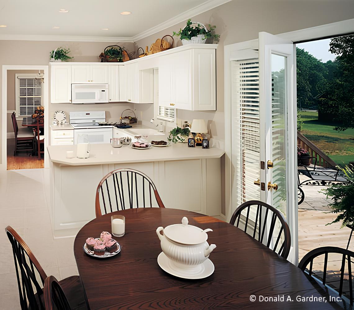 The eat-in kitchen offers white cabinetry, white appliances, a peninsula bar, and an oval dining set.