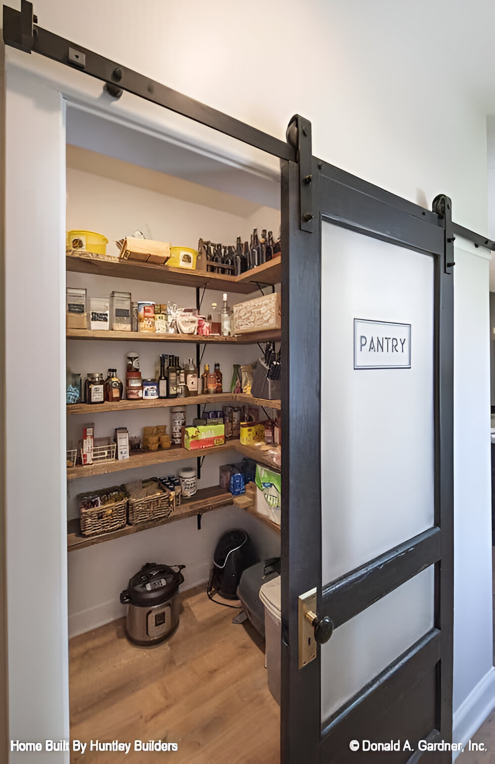 A sliding barn door reveals the walk-in pantry. It is filled with groceries and small kitchen appliances.