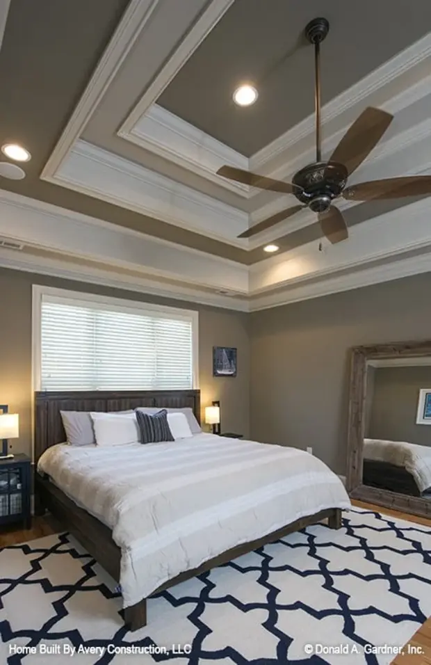 Primary bedroom with a step ceiling, wooden bed, and a full-length mirror placed against the gray walls.