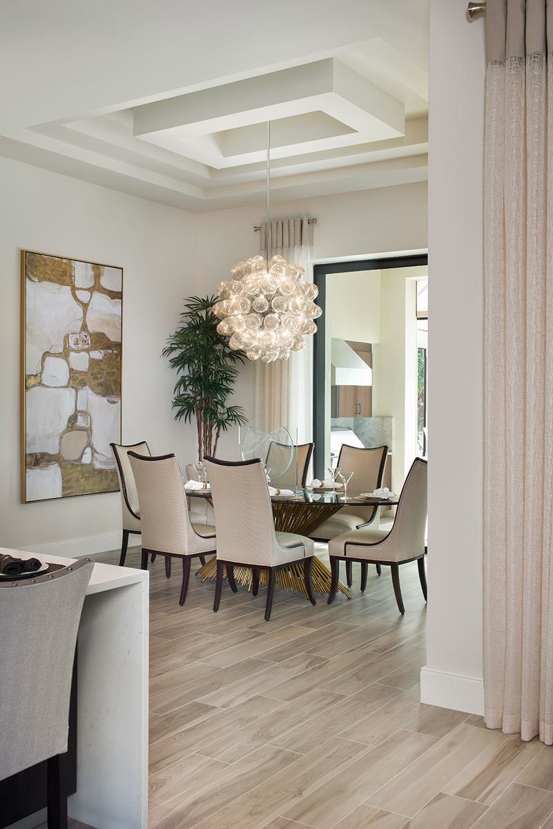 Dining room decorated with a stylish step ceiling, an oversized glass pendant,  and a large artwork mounted against the beige wall.