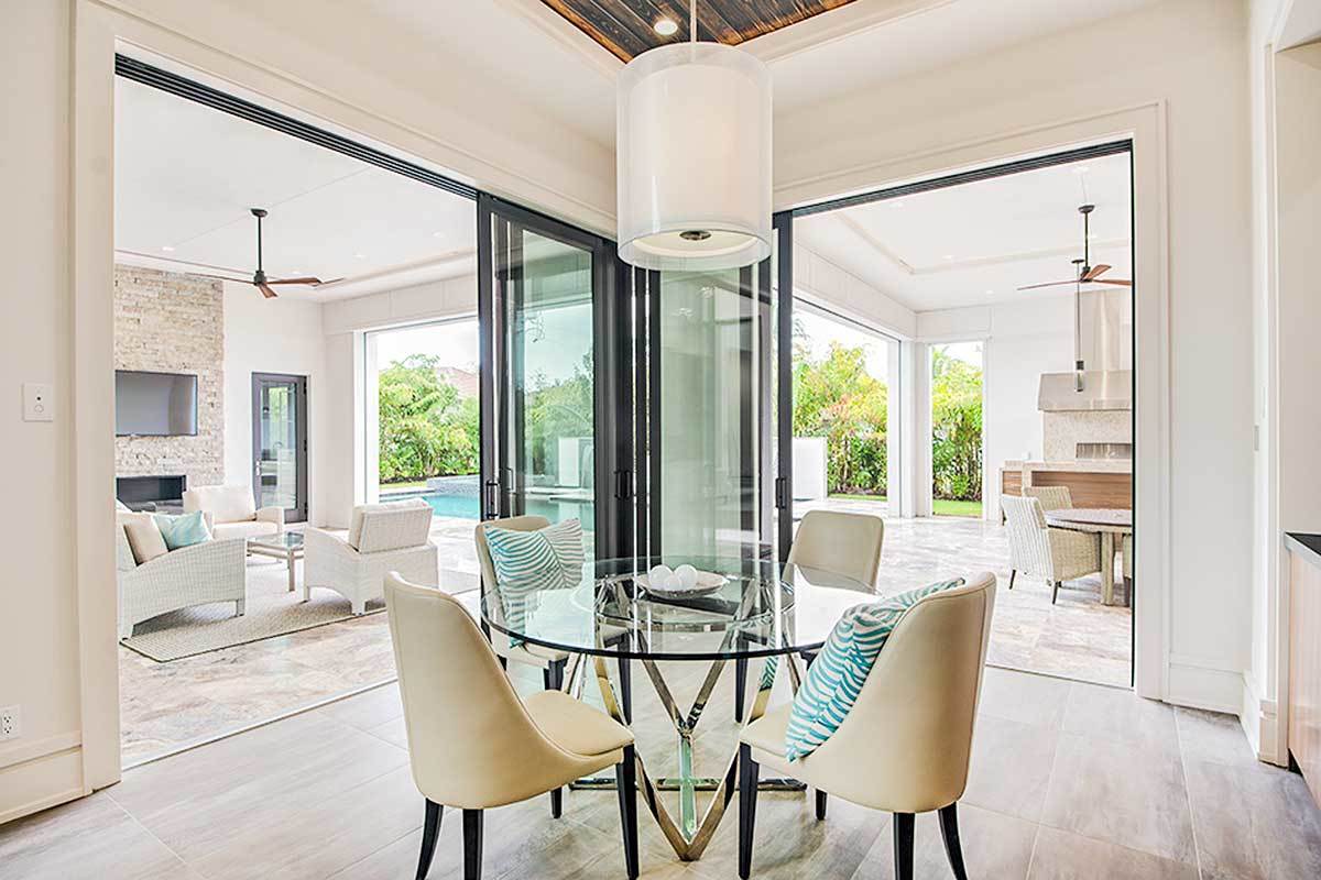 Oversized sliding doors on two sides extend this dining area outdoors. It has a round dining set topped with a cylindrical pendant.