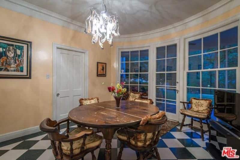 The black and white checkered flooring design goes well with the French glass door and windows that have white frames matching the door and ceiling that are complemented by the yellow walls and the wooden dining set that has an antique quality to it.