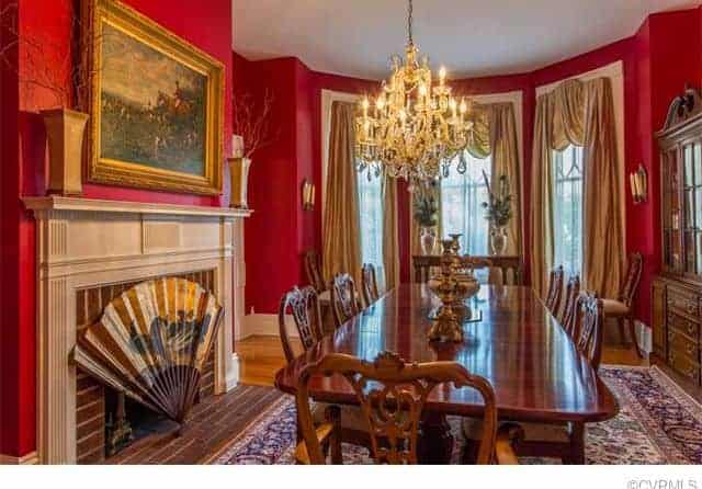 Beside the wooden dining set is a fireplace with red brick inlay and white mantle covered with an oriental decorative large fan that matches the classic painting mounted on the red wall above the mantle. This matches the elegance of the golden chandelier.