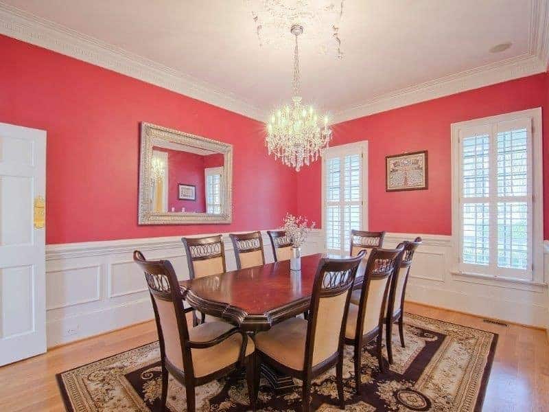 The focal point of this formal dining room is the brilliant crystal chandelier that brightens the white ceiling and white wainscoting. These bright elements are subdued by the pink upper walls that complement the dark wooden dining set.