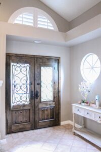 This shabby chic style foyer features a gorgeous wood double-door fitted with glass panels that are framed with ornate metal designs.