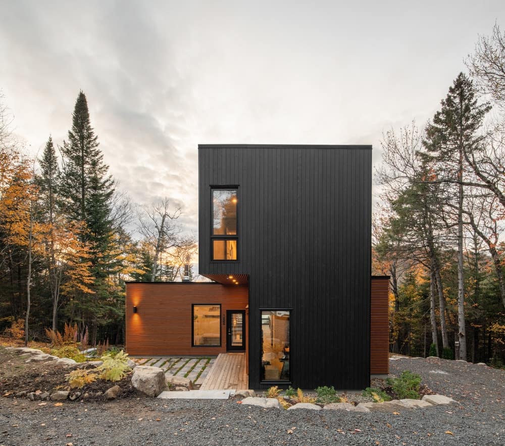 This is a front view of the house that has two tones with wood and black exterior walls complemented by the warm windows.